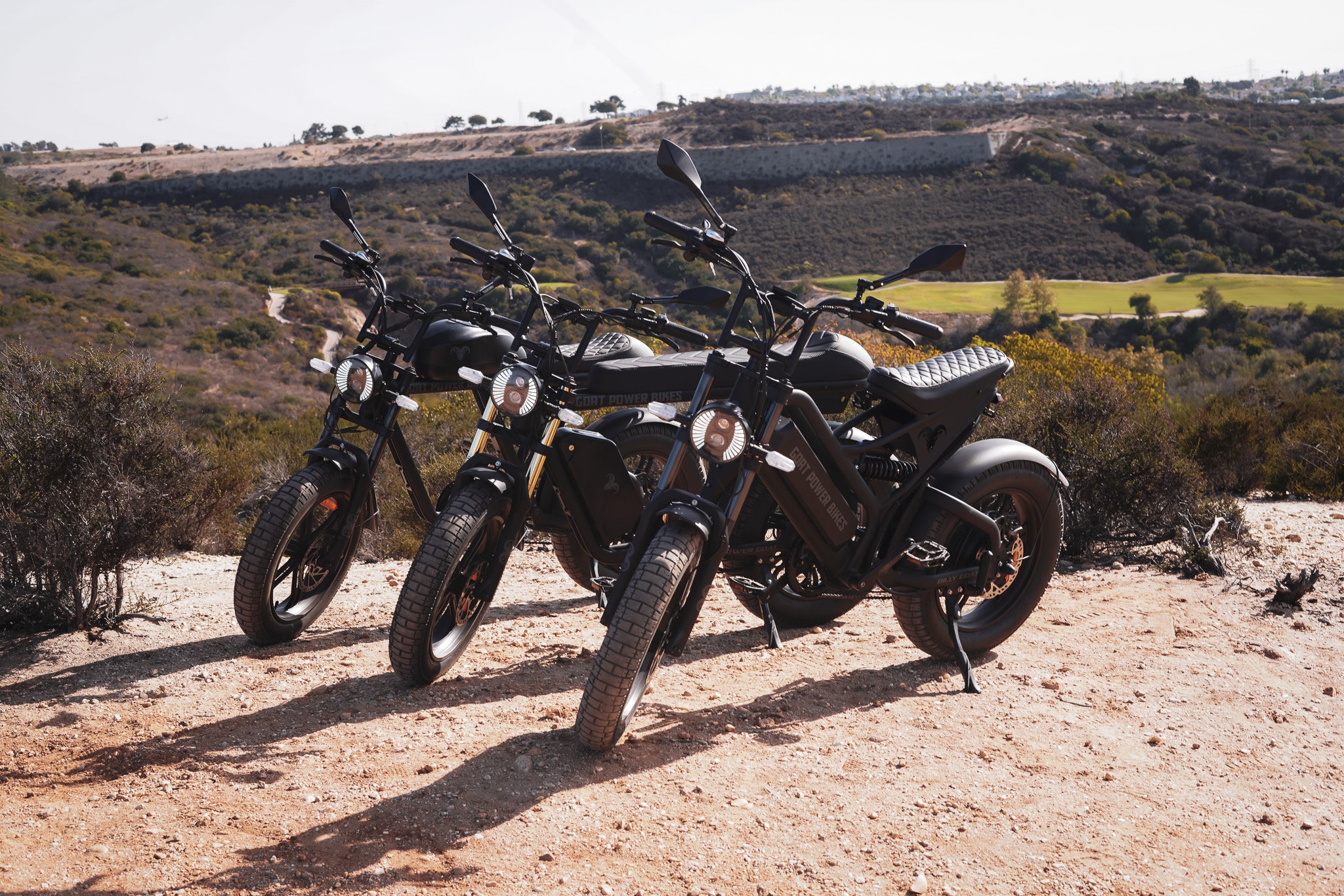 Three electric bikes parked on a dirt road with a scenic background