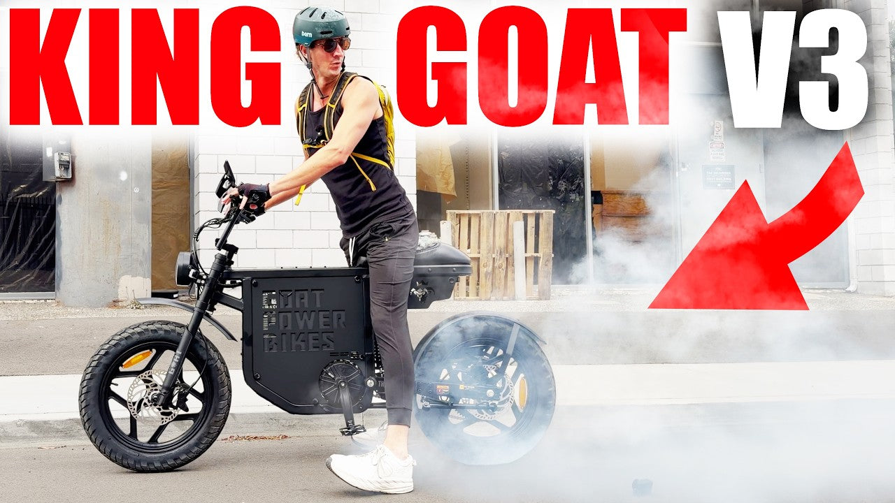 A person wearing a helmet stands beside a Goat Power BIke with large red text reading 'KING GOAT V3' and a red arrow graphic over a smoky urban background.